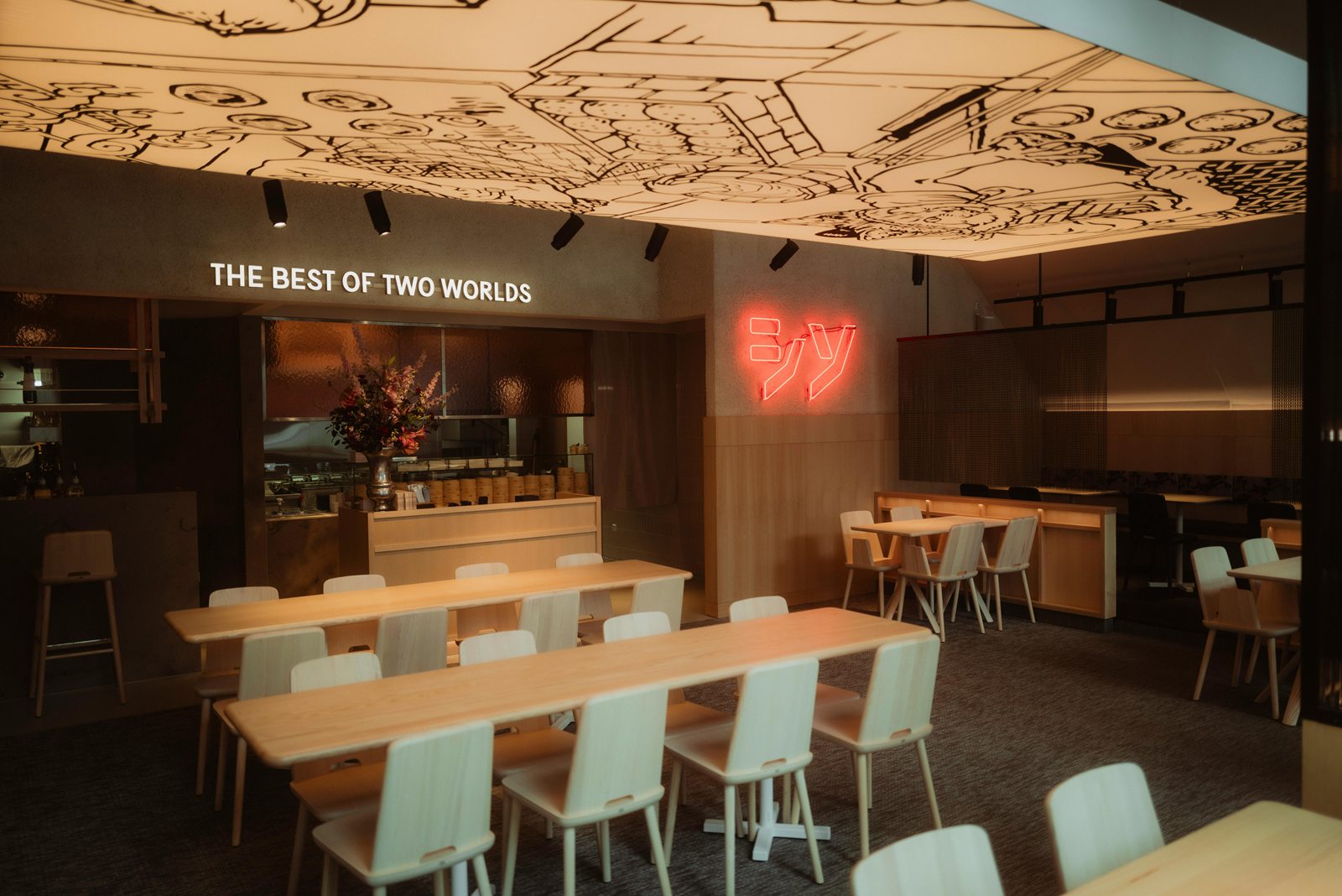 Interieur van Shiso Burger met lichte houten tafels, een plafond vol tekeningen en roze neonletters